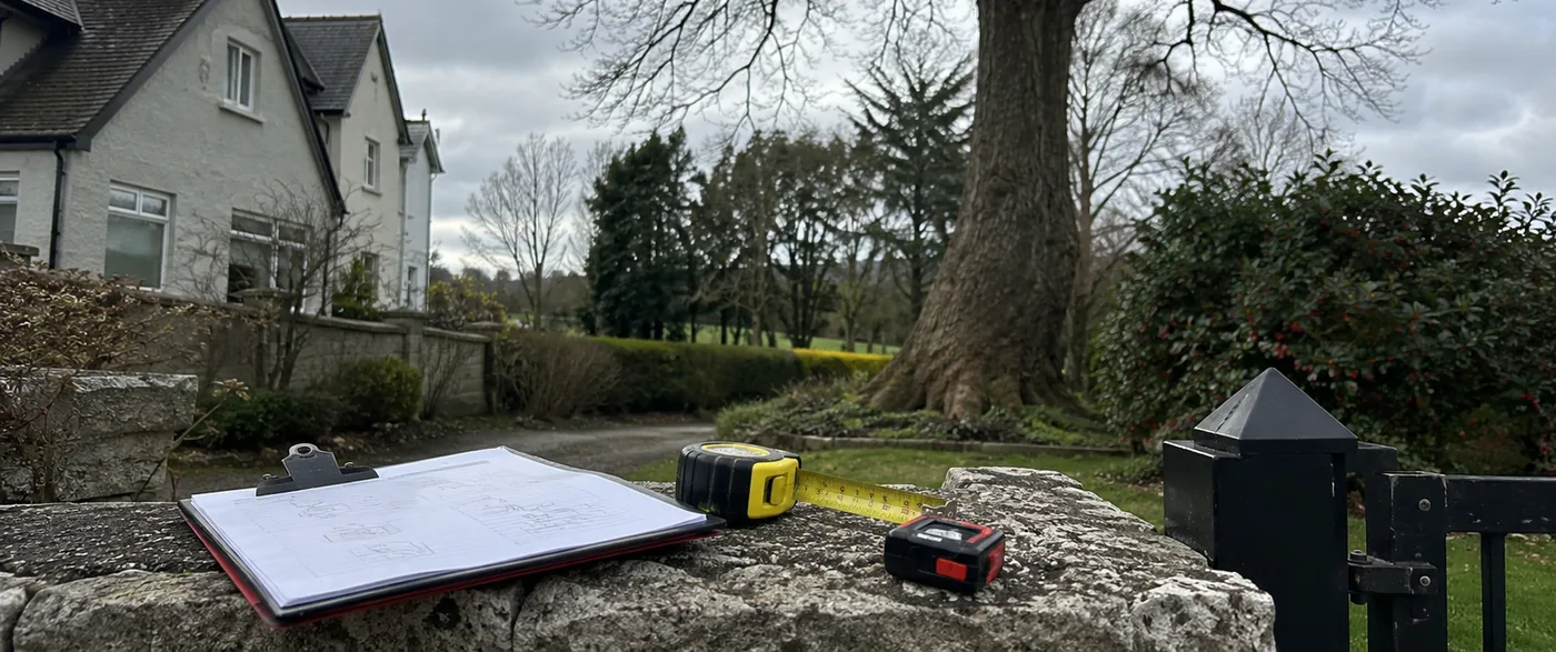 Survey clipboard, tape measure and laser distance meter on a wall in front of a mature tree and house